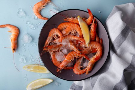 Bowl full of succulent cooked prawns with lemon on blue background with droplets of water. Concept for culinary websites or seafood recipes