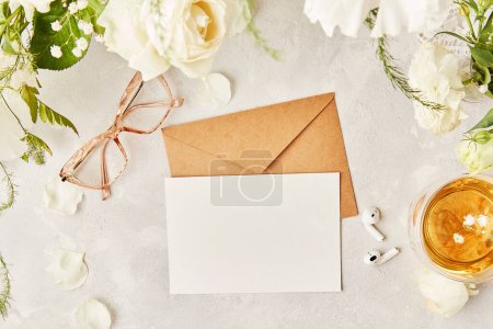 Aesthetic feminine flat lay glasses, tea cup and earphones with crafting paper envelope for greetings, text among white flowers