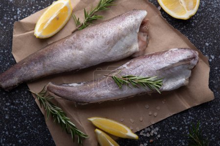 Frischer roher Fisch mit Zitrone und Rosmarin auf dunklem, strukturiertem Hintergrund, perfekt für kulinarische Themen und Gourmetküche