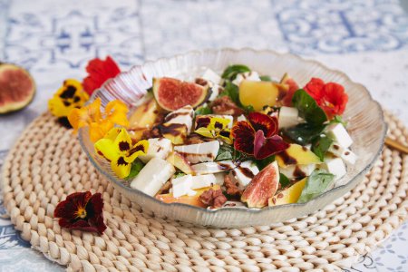 Vegetarian salad with feta, edible flowers, figs, peach, basil on ceramic tile background with sunflowers and pumpkin decorations