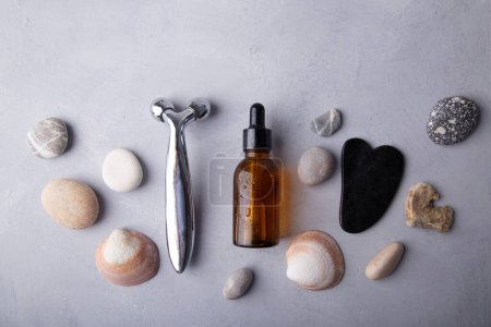 Beauty Essentials und Gesichtsmassagewerkzeuge zwischen Kieselsteinen vor grauem Hintergrund. Sommerbad-Pflegekonzept.