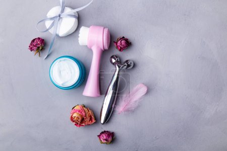 Feminine beauty products. Spa and self-care, face care concept. Face brush, scrub, face massager among dry roses.