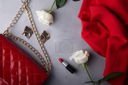 Elegantes accesorios de moda con monedero rojo y productos de belleza clásicos entre rosas.