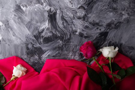 Vibrant roses lying on a textured abstract grey background draped in pink.