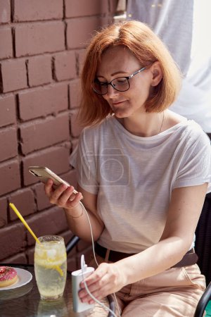 Staying powered up - woman freelancer uses a powerbank to maintain productivity at a cafe.