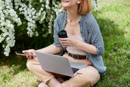 Style de vie indépendant avec ordinateur portable, café et smartphone, femme entourée par la nature tout en travaillant sur son ordinateur portable.