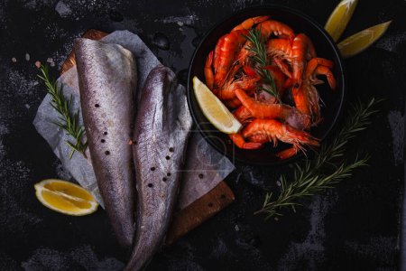 Foto de Arreglo de mariscos frescos con gambas y merluza de pescado sobre fondo oscuro, ideal para presentaciones culinarias. - Imagen libre de derechos