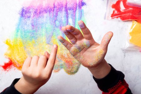 Peinture enfant à la main avec du sable de couleur arc-en-ciel. Touche de couleurs créant un arc-en-ciel abstrait sur la surface blanche.