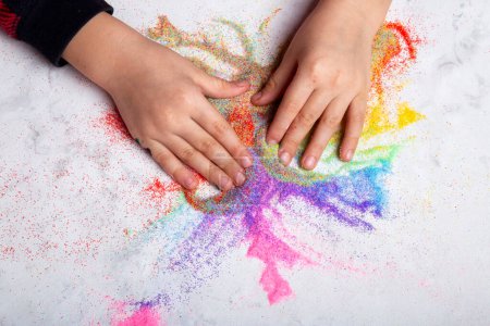 Manos de niño jugando con arena de color arco iris. Habilidades motoras, concepto de creatividad infantil.