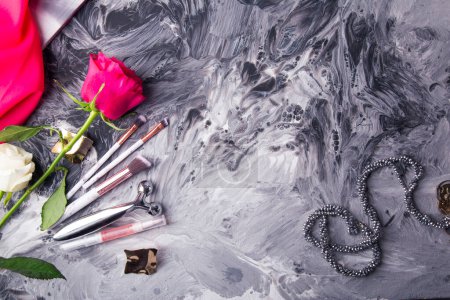 Glamouröse Make-up-Tools und frische Blumen vor einem monochromen, flüssigen Kunsthintergrund.