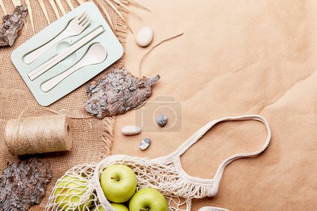 Aesthetic eco-friendly, zero waste, sustainable lifestyle background with reusable bag, cutlery, apples, tree bark, pebbles on crafting paper with copy space