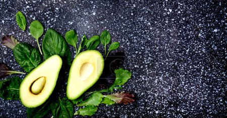 Zusammensetzung aus halbierter Avocado und frischem Blattgemüse - Grundlagen einer gesunden pflanzlichen Ernährung. Extra breites Banner.
