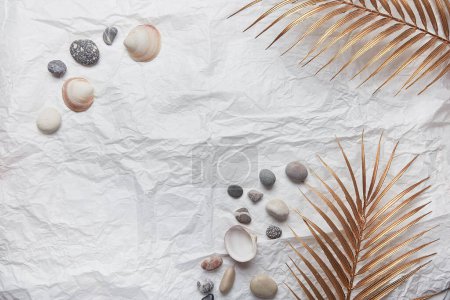 Elegant summer background with golden palm, seashells, pebbles and copy space.