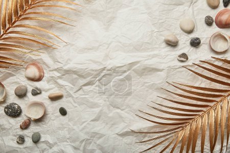 goldenes Palmblatt, Kieselsteine und Muscheln auf sommerlichem Hintergrund mit Kopierraum