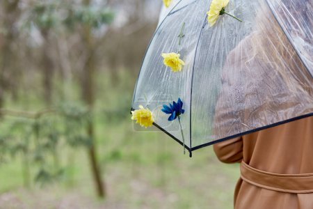 Frau unter permanentem Regenschirm, geschmückt mit frischen Blumen. Symbol für Frühjahrsmode und Regenbekleidungskollektionen. Illustration zur KI