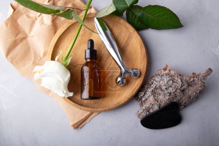 Self care composition with facial serum, gua sha, facial roller. Floral and stone therapy tools for facial rejuvenation on a textured surface.