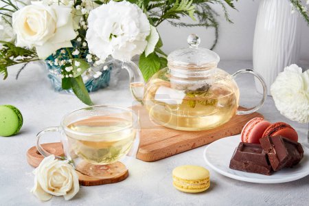 Morning aesthetic table. Teapot, cup, macaroon desserts, chocolate, white flowers - time for yourself, enjoy your time concept.