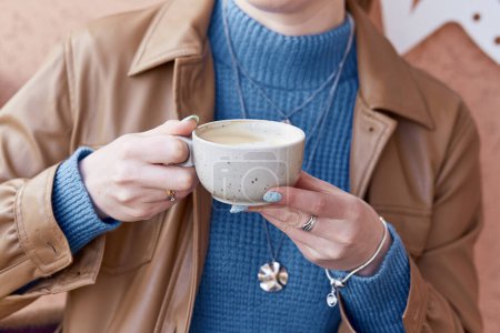 Femme avec manucure bleue tient une tasse de café de près.