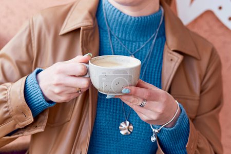 Femme avec manucure bleue tient une tasse de café de près.