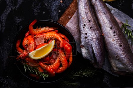Foto de Surtido de mariscos crudos, langostinos y pescados de merluza con limón y hierbas para platos visuales de menú de restaurante - Imagen libre de derechos