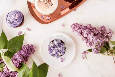 Ajuste de mesa estética primavera. Pastelitos franceses púrpura en la bandeja de oro, taza de café y flores lila plana laico