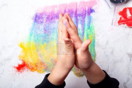 Little fingers playing with vibrant sand on white background. Motor skills, child creativity concept.