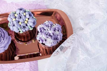 Vue de dessus des cupcakes floraux violets esthétiques avec une tasse de café. Pas de dessert sucré parmi les fleurs lilas.