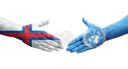 Poignée de main entre les drapeaux des Nations Unies et des îles Féroé peints sur les mains, image transparente isolée.