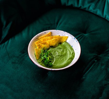 Photo for Homemade broccoli cream soup in white bowl with chips on green velvet background - Royalty Free Image