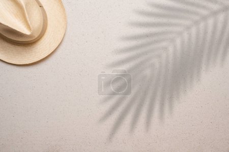 Summer, beach and vacation concept with free text space. Top view. Flat layout with a man straw hat in the upper left corner on a fine sandy background and with a palm leaf shade in the right side