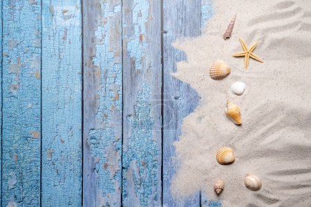 Sommer-, Strand- und Urlaubskonzept mit Freitextfläche. Ansicht von oben. Flaches Layout mit verschiedenen Muscheln und feinem Sand am Strand auf altem, blauem Holzbrett