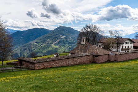 Foto de Una antigua granja vallada con paredes de ladrillo frente a un impresionante paisaje de montaña - Imagen libre de derechos
