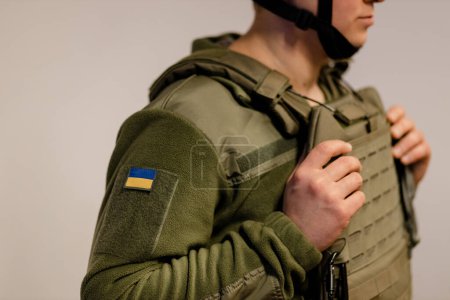 Téléchargez les photos : Forces armées ukrainiennes. Soldat ukrainien se tient debout et tient la main sur le gilet pare-balles. Armée ukrainienne. Drapeau ukrainien sur uniforme militaire. - en image libre de droit
