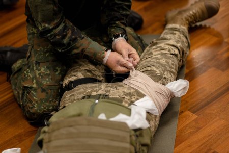 Téléchargez les photos : Entraînement habillage de la jambe blessée d'un combattant ukrainien, gros plan. Vue d'en haut. Photo de haute qualité - en image libre de droit