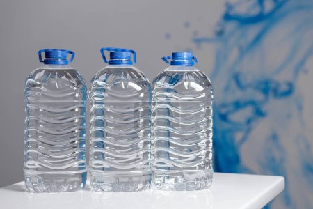 Téléchargez les photos : Three full 5 liter bottles of water on a white table on a gray background. Water delivery. High quality photo - en image libre de droit