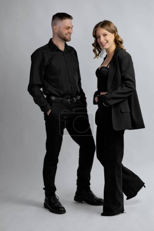 Téléchargez les photos : Jeune femme et jeune homme en vêtements noirs souriant toute la longueur en studio. Photo de haute qualité - en image libre de droit