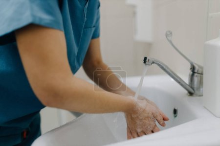 Téléchargez les photos : Image en gros plan des mains d'une travailleuse médicale se lavant méticuleusement avec de l'eau. Cette prise de vue détaillée reflète le dévouement à l'hygiène et aux soins aux patients. - en image libre de droit