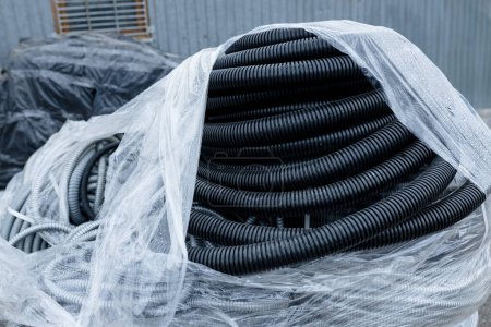 Téléchargez les photos : Tuyaux industriels noirs empilés et enveloppés dans du plastique, prêts à être expédiés ou installés. - en image libre de droit