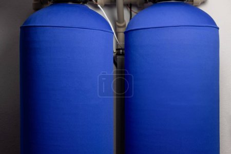 Two blue water softener tanks stand side by side, connected with pipes in a utility room.