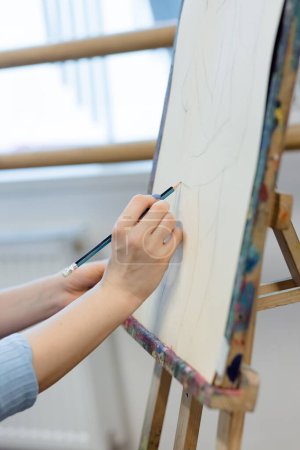 Photo for Close-up shot of an artists hands skillfully sketching on a canvas. The canvas is placed on a color-stained easel in a bright art studio. - Royalty Free Image