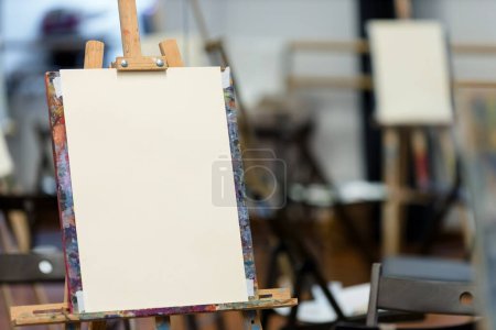Foto de Un lienzo en blanco sobre un caballete de colores en un estudio de arte, listo para pintar, con otro lienzo en el fondo. - Imagen libre de derechos