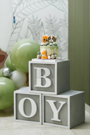 A charming setup featuring BOY spelled with large blocks, topped with a cute cake adorned with toy animals. Green and silver balloons complement the scene