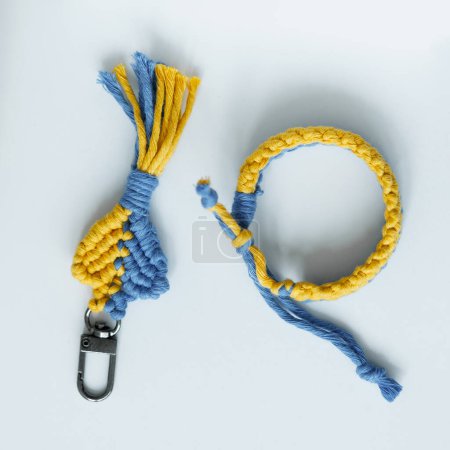 Un vibrante llavero de macramé artesanal y un conjunto de brazaletes, con una hermosa interacción de hilos azules y amarillos, exhibidos sobre un fondo blanco prístino