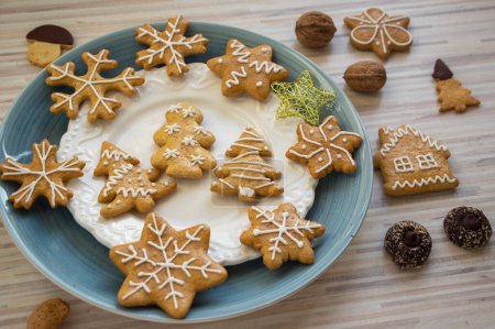 Photo for Painted traditional Christmas gingerbreads arranged on blue and white plates on light wooden table in daylight, various xmas shapes trees, stars and snowflakes - Royalty Free Image