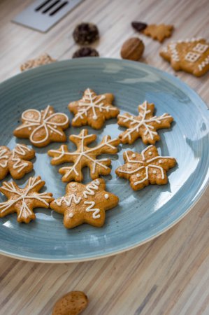 Photo for Painted traditional Christmas gingerbreads arranged on blue plate on white wooden table in daylight, various xmas shapes trees, stars and snowflakes and chocolate buttons - Royalty Free Image
