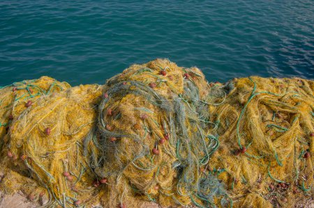 Téléchargez les photos : Pêcheurs équipement couché sur le littoral dans le port, tas nylon jaune emmêlé filet de pêche en Grèce lumière du soleil - en image libre de droit