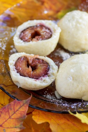 Téléchargez les photos : Boulettes de prunes coupées en deux dans l'assiette sur de vraies feuilles automnales colorées avec glaçage au sucre blanc, cuisine tchèque savoureuse - en image libre de droit