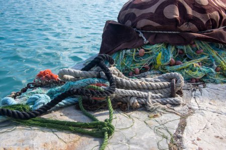 Téléchargez les photos : Pêcheurs équipement couché sur la côte dans le port, tas nylon jaune filet de pêche emmêlé dans la lumière du soleil grecque, cordes colorées - en image libre de droit