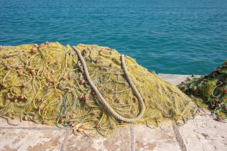 Téléchargez les photos : Pêcheurs équipement couché sur le littoral dans le port, tas nylon jaune emmêlé filet de pêche en Grèce lumière du soleil - en image libre de droit