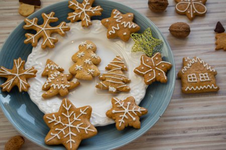 Téléchargez les photos : Pains d'épice de Noël traditionnels peints disposés sur des assiettes bleues et blanches sur une table en bois clair à la lumière du jour, diverses formes de Noël arbres, étoiles et flocons de neige - en image libre de droit